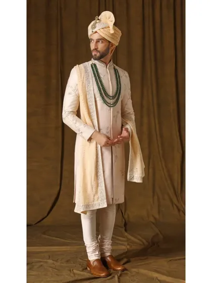 The Jashn-e-Ada sherwani in a soft blush peach. The handwoven fabric is adorned with captivating threadwork and a touch of gold, embodying contemporary regal charm.