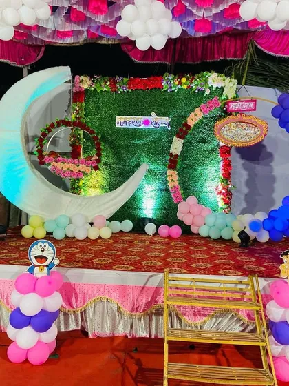 A naming ceremony stage with two moon props, a cradle, and various cartoon character cutouts.