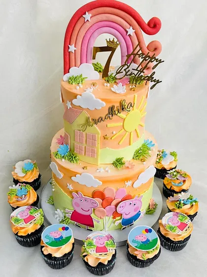 A cheerful two-tier Peppa Pig cake, perfect for a sunny 7th birthday. This design features a warm sunset color palette, a rainbow topper, and adorable edible prints of Peppa and George, complete with matching themed cupcakes.