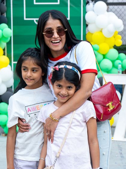A mother and her daughters smile for the camera, enjoying the festive atmosphere of the outdoor football party.