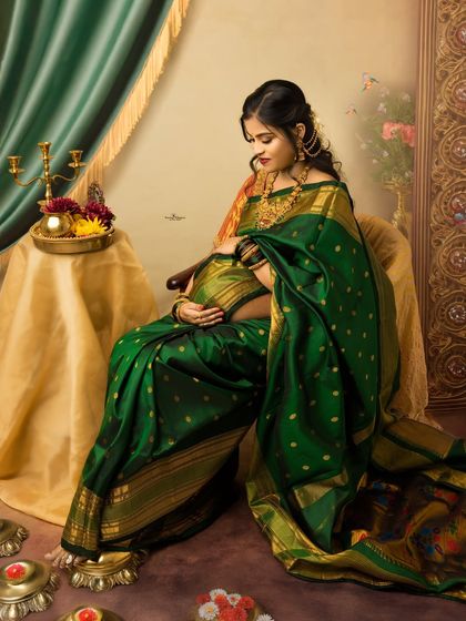 A full-length solo portrait capturing the elegance of a traditional twin pregnancy photoshoot. The rich green saree and classic setting create a timeless piece of art.