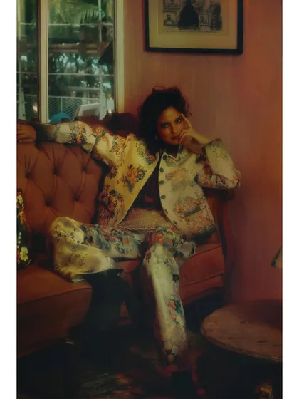 From 'Chapter 6: Collision of Thens'. The styling features a full suit with a soft, floral-adjacent pattern. The relaxed, almost masculine pose signifies a newfound confidence.