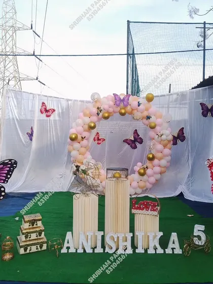 An outdoor butterfly-themed 5th birthday party with a circular balloon arch and props.