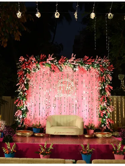 A stage that glows with glamour. The shimmering pink sequin backdrop, framed with lush flowers, creates a vibrant and celebratory atmosphere perfect for a sangeet or reception night.