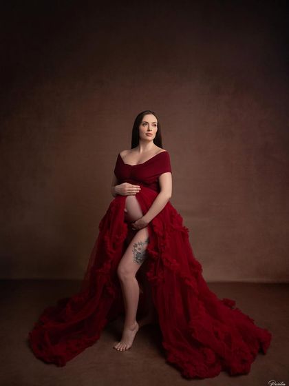 A powerful and artistic pose in a deep red gown against a classic brown backdrop. The open front and flowing train create a dramatic, goddess-like image.