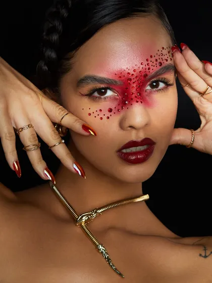A red muse. This stunning creative look features a mask of red rhinestones across the eyes, paired with a bold red lip.