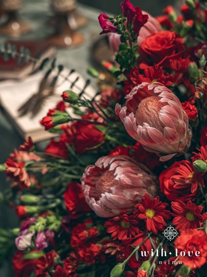 A close-up of a lush, deep red floral arrangement featuring proteas and roses. The rich colors and textures were chosen to complement the dramatic and romantic theme of the sangeet.