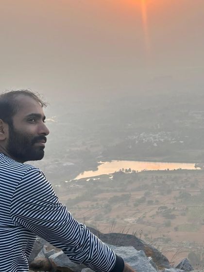 A trekker looking out at the view, with the sun reflecting in a distant lake. It's a serene and picturesque moment.