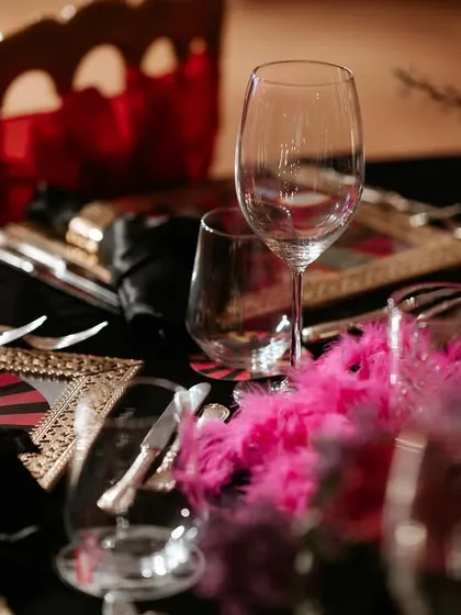 A close-up of a themed table setting from an event in Antalya. The combination of black, red, and gold with playful pink feathers created a glamorous and unique Moulin Rouge-inspired aesthetic.