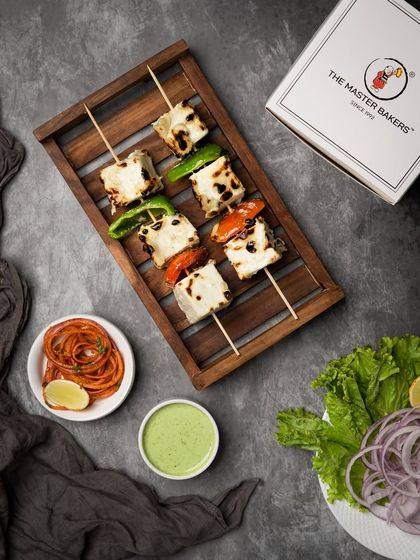 Our classic Paneer Tikka, featuring soft cubes of paneer marinated in yogurt and spices, then grilled with bell peppers and onions. This overhead shot shows the dish ready to be served from our signature takeaway box.