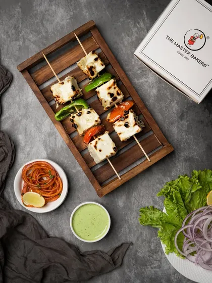Our classic Paneer Tikka, featuring soft cubes of paneer marinated in yogurt and spices, then grilled with bell peppers and onions. This overhead shot shows the dish ready to be served from our signature takeaway box.