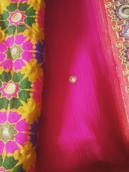 This image shows a combination of fabrics for a festive outfit. On the left is a colorful phulkari-style embroidered fabric with mirror work, paired with a sheer pink georgette that has a detailed embroidered border.