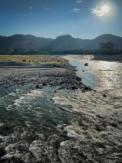 A bright, sunny day on the river in Jim Corbett, with the water churning in the foreground. This image captures the energy of the river and the vastness of the surrounding landscape.