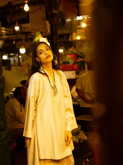 A portrait in a dimly lit market, using the ambient light from the bulbs to create a warm, atmospheric glow. The out-of-focus foreground adds depth.
