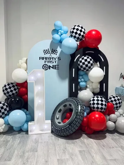 A "Fast One" race car theme for a first birthday. The setup includes a light-up number "1", a tire prop, and a balloon garland with checkered flag details.