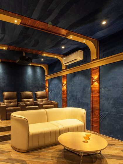 The home theatre in the "Opulent Abode" is designed for a luxurious cinematic experience, with plush seating, acoustic wall paneling, and a rich blue and wood color scheme.