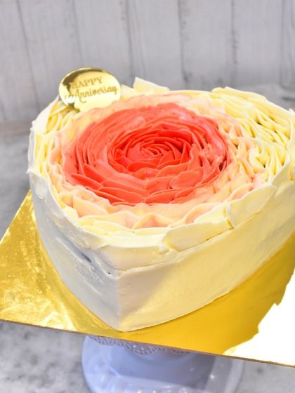 A beautiful heart-shaped anniversary cake with a piped rosette design. The colors blend in an ombre effect from red to orange to yellow, creating a warm and romantic look.
