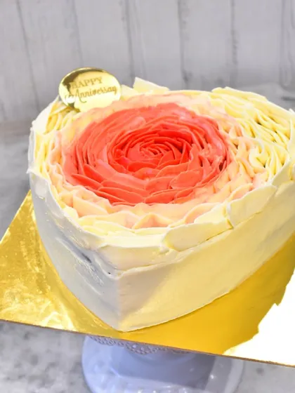 A beautiful heart-shaped anniversary cake with a piped rosette design. The colors blend in an ombre effect from red to orange to yellow, creating a warm and romantic look.