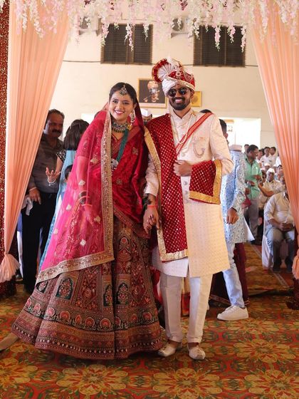 A happy bride and groom making their entrance as a married couple. She is glowing in a beautiful multi-toned bridal lehenga, perfectly complementing his sherwani.