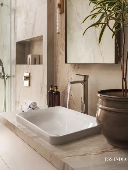 A close-up on the vanity area, showing the clean lines of the vessel sink and chrome faucet. Rolled white towels and amber soap dispensers add a spa-like finishing touch.