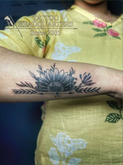 A beautiful sunflower tattoo designed as a forearm band, with leaves extending outwards.