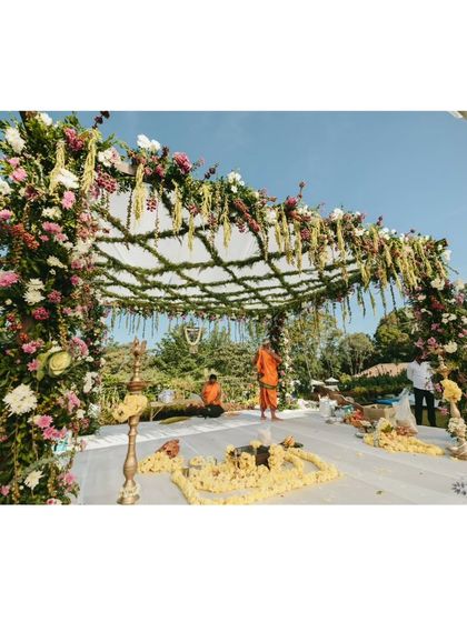 A side angle of the coffee berry mandap, highlighting the lush floral arrangements on the pillars against a clear blue sky.