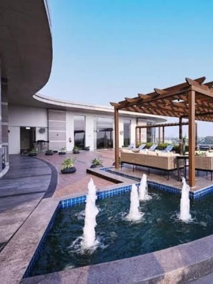 A beautiful water feature with multiple fountains adds a dynamic and refreshing element to this hotel's outdoor area, complementing the poolside pergola and lounge seating.
