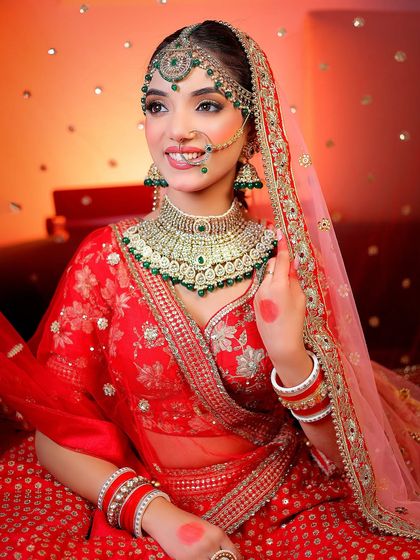 A radiant bride in a traditional red lehenga with green jewelry. The warm lighting and bokeh background make this portrait pop.