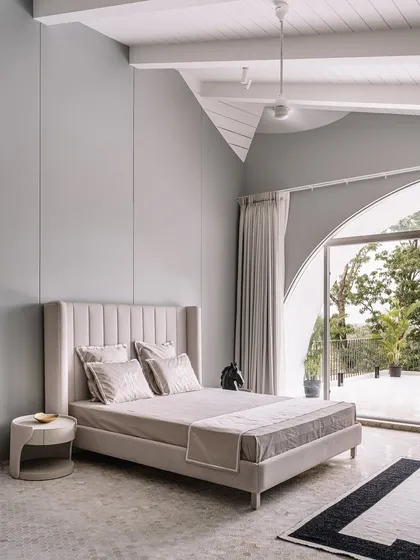 Neutral tones have the power to create a serene retreat. In this bedroom, I paired a soft grey palette with a statement arched window and a high-backed upholstered bed to craft an atmosphere of understated tranquility.