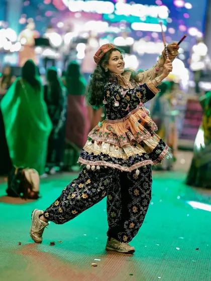 A young girl in full traditional attire dances with dandiya sticks, her joyful expression capturing the spirit of Navratri.