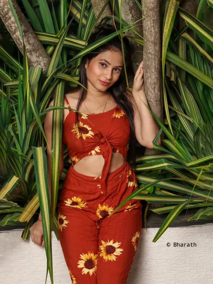 A three-quarter shot of the model leaning against a tree, framed by variegated leaves that complement the shot.