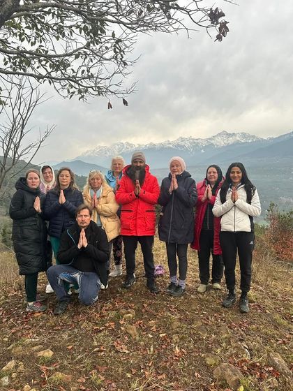 A group of students and I in Anjali Mudra (prayer hands) on a hilltop, with the majestic snow-capped Himalayas in the background. We offered our gratitude for the mountains and the practice.