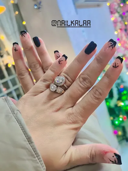 A reverse French manicure with a black base and delicate palm tree art on the nail bed. This is a unique and creative design, perfect for a vacation-ready look.