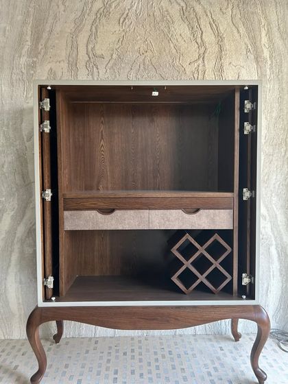 The bar cabinet opens to reveal a fully functional interior with wine storage and drawers, crafted from warm wood that contrasts beautifully with the painted exterior.