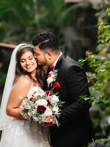 A sweet and tender moment between the newlyweds. The groom's gentle kiss on his bride's cheek is a simple gesture filled with love and affection, captured in soft, natural light.