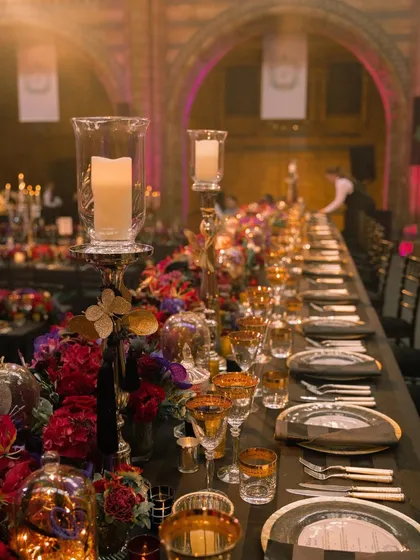 A long-table view of the dramatic and moody reception decor. The combination of dark linens, candlelight, and rich florals is perfect for a glamorous evening event.