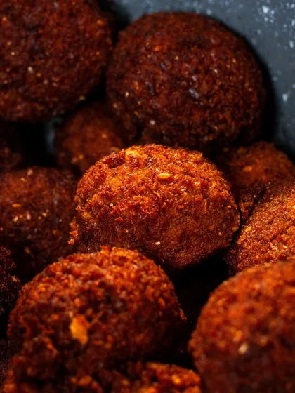 A macro shot of freshly fried falafel. The detail on the crispy exterior is incredibly appetizing and perfect for showcasing a popular vegan option.