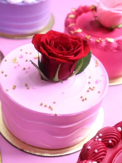 A collection of our mini cakes for Rose Day, each one a different shade of pink and purple and topped with a beautiful red rose. It's a garden of sweet delights.