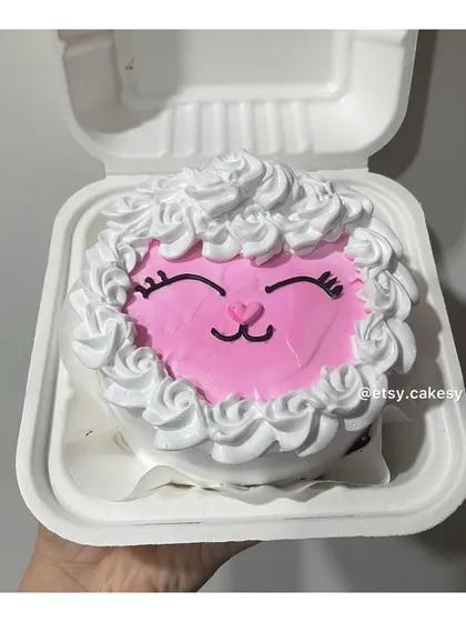 An adorable sheep-themed bento cake. The face is made with pink frosting and the wool is piped with white frosting rosettes.