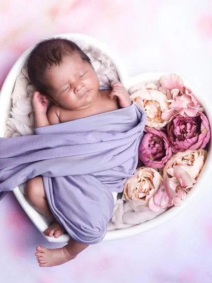 A beautiful pose with a baby partially wrapped in a lavender cloth, sleeping in a heart-shaped bowl filled with flowers.