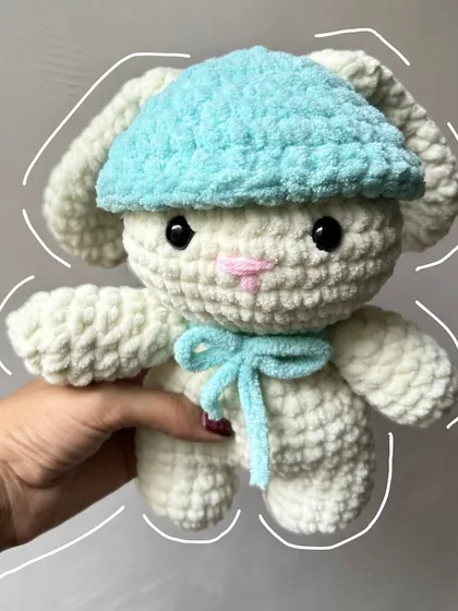 A super soft and cuddly crochet bunny plushie with a cute blue hat and bow, ready for hugs.