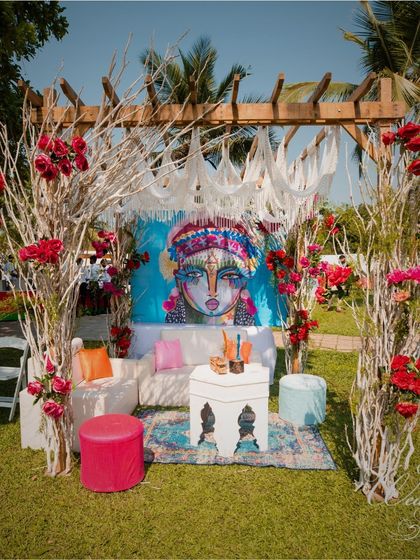 A perfect example of our bohemian-chic decor. We created this beautiful Mehendi seating area with a backdrop of a modern art piece, framed by white-washed branches and pops of red roses.