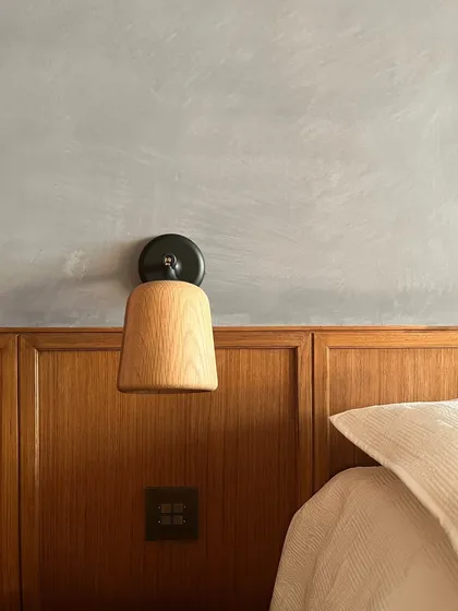 A wall-mounted bedside lamp is perfectly integrated with the wooden dado and limewashed wall. The simplicity of the fixture complements the rich textures of the wall treatments.