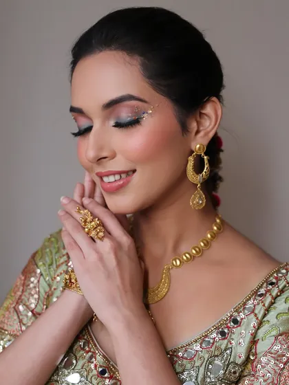 A beautiful, gentle pose highlighting the artistic eye makeup and stunning gold jewelry. This shot shows how the makeup complements the traditional accessories for a cohesive look.