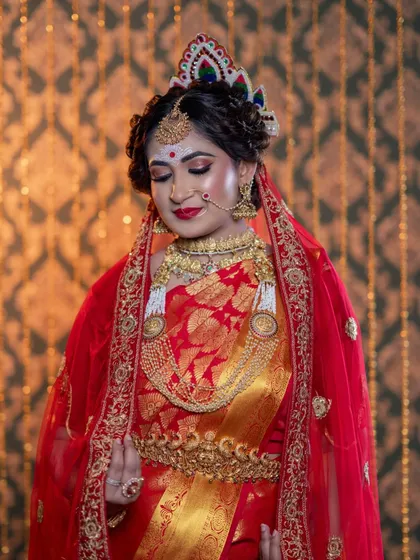The bride is draped in a red veil, a classic element of the Bengali wedding. The makeup, especially the eyes and lips, stands out beautifully.