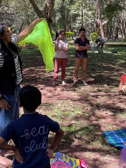 A guest storyteller uses a bright green scarf to demonstrate movement. Props like play silks are fantastic for encouraging creative expression and physical activity.