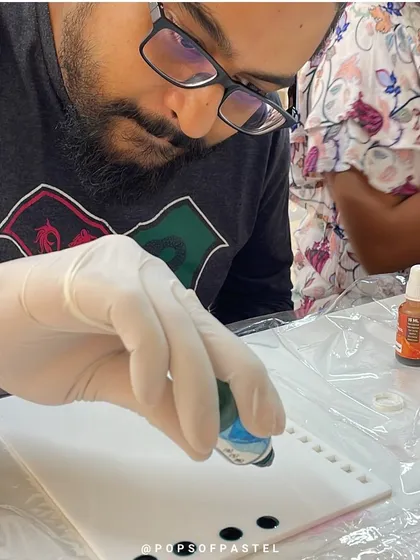 A close-up of a participant dropping alcohol ink onto the surface, the first step in creating a vibrant design.
