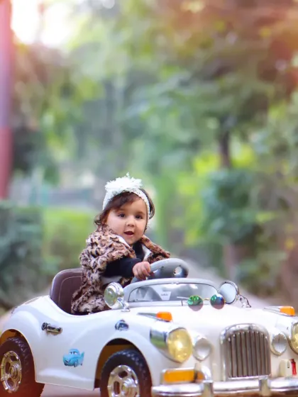 A little girl looking chic in her toy car during an autumn-themed outdoor shoot. The fallen leaves add beautiful color and texture to the scene.