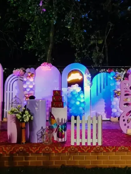 An outdoor butterfly-themed birthday setup at night. The lighting on the pink and purple decor creates a magical and enchanting atmosphere for the celebration.
