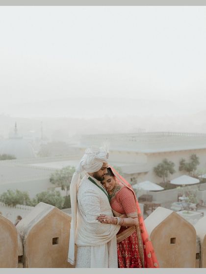 An embrace that feels like coming home. The couple holds each other close on a balcony overlooking the hazy, romantic landscape of Udaipur, a quiet moment of love and contentment.